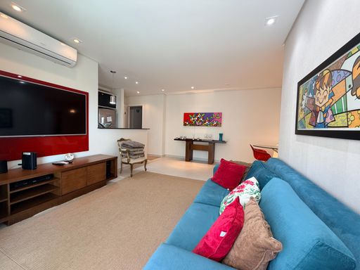 Sala ampla com decoração moderna
Sala de estar e jantar conjugadas com sofás e quadros decorativos.
Uma visão panorâmica do living mostra o sofá azul em primeiro plano com almofadas vermelhas e estampadas, criando um belo contraste cromático. O tapete de tom neutro unifica o ambiente de convivência, que conta com quadros artísticos nas paredes e um ar-condicionado split. Ao fundo, avista-se a abertura para a cozinha americana, proporcionando uma transição suave entre os ambientes com uma estética urbana, arejada e sofisticada.