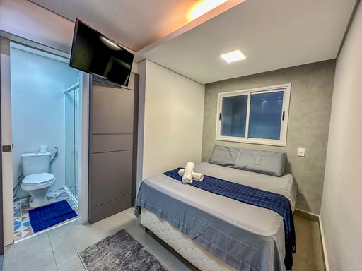 Perspectiva do quarto máster.

Quarto de casal com armário embutido, painel ripado e ar-condicionado.

Uma visão lateral do dormitório que mostra o armário planejado em tom cinza escuro, otimizando o armazenamento. A cabeceira ripada e as paredes de cimento queimado reforçam a unidade visual industrial do apartamento. O ar-condicionado e a iluminação em LED no teto garantem praticidade e conforto. A entrada para o banheiro privativo é visível, demonstrando a funcionalidade da suíte. A estética é sóbria e sofisticada, perfeita para um ambiente de repouso moderno.