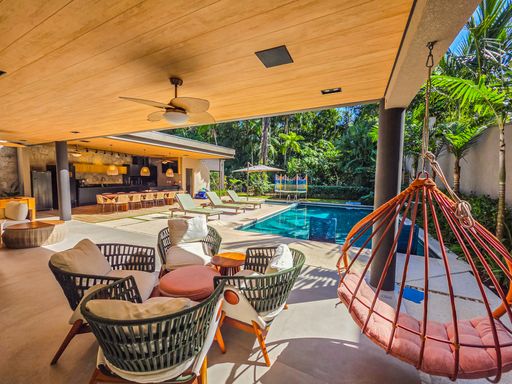 Lounge externo de luxo

Espaço de estar ao ar livre com poltronas, balanço suspenso e piscina.

Este lounge de lazer integra-se totalmente à piscina através de um deck nivelado. O mobiliário inclui poltronas de fibra sintética e um icônico balanço suspenso em tom coral que traz um ponto de cor vibrante. O forro de madeira do teto estende-se para a área de estar, unificando os espaços cobertos e descobertos. Cercado por vegetação densa e sob a sombra de árvores, o ambiente oferece uma estética tropical elegante e uma sensação térmica de refúgio sombreado.