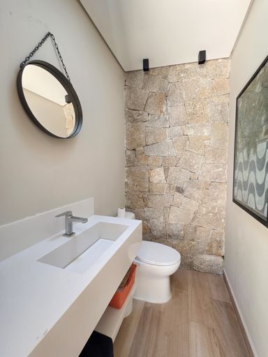 Banheiro de spa privativo

Lavabo de SPA com cuba esculpida, espelho redondo e parede de pedra.

Este banheiro sofisticado combina uma bancada branca de linhas retas com uma imponente parede de fundo em pedra natural irregular. Um espelho redondo com moldura escura e uma tela de arte contemporânea trazem design ao espaço. O piso segue o padrão amadeirado de toda a área de bem-estar, mantendo a unidade visual. A estética é de um refúgio de autocuidado, com iluminação indireta que proporciona uma sensação térmica de calma e frescor mineral.