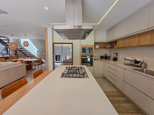 Perspectiva de cozinha e estar

Visão da ilha gourmet em direção ao living e áreas de circulação.

Este ângulo mostra a fluidez entre a área de preparo de alimentos e as demais zonas sociais da residência. O mobiliário planejado integra-se à arquitetura, utilizando materiais como quartzo branco, madeira clara e aço inoxidável. O piso cerâmico acetinado reflete suavemente a iluminação do teto, ampliando a sensação de espaço. A estética é de organização absoluta e modernidade, proporcionando uma sensação térmica de conforto e arejamento por todo o pavimento térreo.