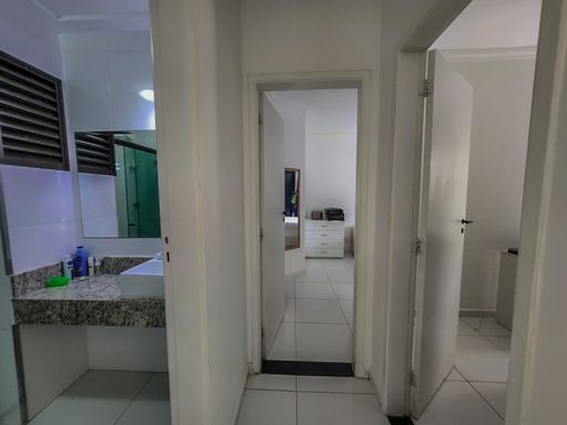Corredor de acesso e banheiro

Visão de um corredor interno interligando o banheiro e outros cômodos.

Corredor de circulação interna de um apartamento com piso cerâmico claro e paredes brancas. À esquerda, avista-se a entrada de um banheiro social com bancada de granito salpicado, pia de sobrepor branca e um grande espelho fixado na parede. O corredor segue em frente revelando portas de madeira pintadas de branco que dão acesso aos quartos. A iluminação artificial superior garante clareza na transição entre os ambientes, mantendo a unidade estética minimalista e funcional do imóvel.