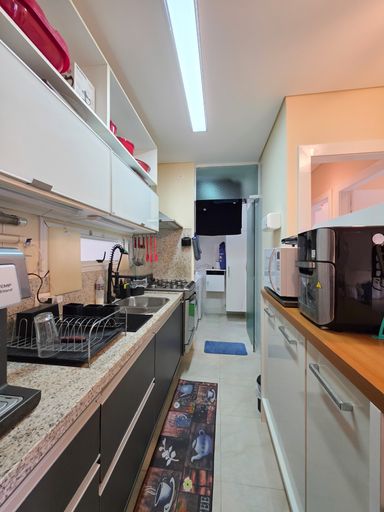Cozinha moderna com eletrodomésticos

Bancada de granito com pia de inox, armários planejados e eletrodomésticos.

Perspectiva interna da cozinha funcional focando na área de preparo. A bancada de granito cinza-claro possui uma pia embutida com escorredor de pratos preto e uma torneira flexível moderna. Os armários planejados superiores em MDF branco contrastam com as gavetas escuras inferiores. Utensílios de cozinha vermelhos estão pendurados de forma organizada na parede ao fundo. Do lado direito, uma bancada branca com tampo de madeira acomoda uma fritadeira elétrica e um forno de micro-ondas, garantindo praticidade ao dia a dia.