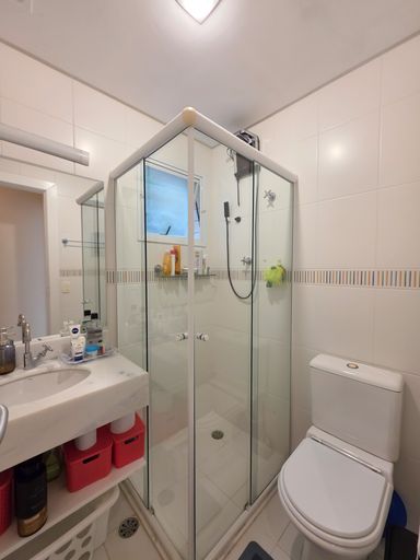 Banheiro social moderno e funcional

Banheiro com box de vidro blindex, pia de louça branca e espelho.

Um banheiro social compacto e muito bem distribuído. O espaço possui revestimento cerâmico branco com uma faixa de pastilhas decorativas horizontais em tons neutros. O box de canto com portas de correr de vidro temperado otimiza a área de banho, que conta com uma janela basculante para ventilação natural. Uma bancada suspensa de louça branca abriga a pia e suporta produtos de higiene pessoal, acompanhada por um espelho retangular fixado na parede. Organizadores plásticos vermelhos sob a pia adicionam um toque de cor.