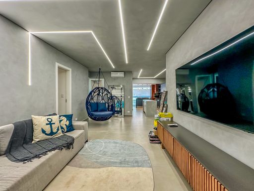 Sala de estar moderna industrial.

Sala de estar com paredes de cimento queimado, iluminação em fitas de LED no teto e poltrona suspensa azul.

Este living contemporâneo aposta na estética industrial com paredes em cimento queimado e um projeto luminotécnico minimalista de fitas de LED embutidas. O mobiliário inclui um sofá cinza de tecido macio decorado com almofadas náuticas e uma poltrona suspensa em fibra azul, que atua como peça de design central. O rack em madeira ripada traz aconchego térmico, equilibrando o piso frio em tons de cinza. A iluminação é difusa e moderna, criando uma atmosfera urbana e sofisticada ideal para apresentações de imóveis de alto padrão.