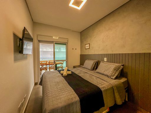 Quarto de casal iluminado.

Cama de casal vista de frente com painel ripado e TV na parede.

A imagem apresenta o quarto de casal em toda a sua extensão, focando no conforto e na tecnologia. A TV está instalada em frente à cama box, em uma parede de cimento queimado com iluminação suave. O painel ripado atrás da cama adiciona textura e elegância. O teto claro reflete a iluminação central, garantindo um ambiente vibrante durante o dia. A sensação térmica é equilibrada pela climatização e pela escolha de tecidos confortáveis, resultando em uma estética de hotelaria de luxo.