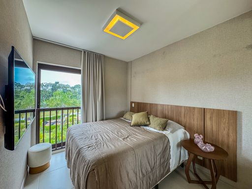 Quarto de Casal Conchegante

Dormitório de casal com enxoval branco e iluminação cênica.

Quarto de casal sofisticado decorado em paleta de cores neutras e suaves. A cama box de casal está vestida com enxoval branco impecável e ladeada por uma mesa de cabeceira branca com gaveta. O painel da cabeceira se estende pela parede, encimado por um quadro decorativo centralizado. No teto, pontos de luz embutidos (spots) criam um efeito de iluminação cênica e relaxante nas paredes. Cortinas brancas cobrem a janela, promovendo privacidade, conforto acústico e sensação estética de tranquilidade.