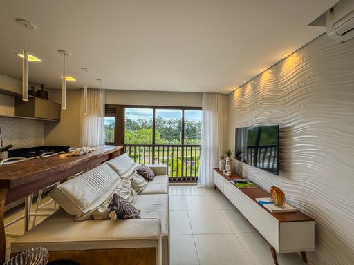Sala de Estar Acolhedora

Sala de estar com sofá bege e painel de TV em madeira.

Uma confortável sala de estar mobiliada com um sofá de couro claro decorado com almofadas estampadas. À frente, um rack de madeira de demolição dá suporte à televisão, complementado por um garden seat amarelo de cerâmica. Grandes portas de vidro de correr oferecem ampla iluminação natural e conectam o espaço diretamente à varanda. O teto rebaixado em gesso possui luminárias embutidas que criam uma atmosfera aconchegante e relaxante.