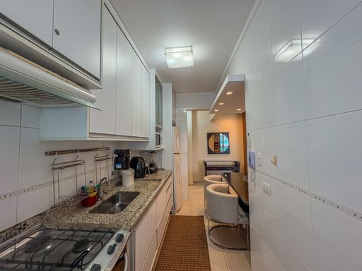 Cozinha planejada em estilo corredor

Bancada de granito com pia integrada a armários brancos e mesa.

Perspectiva interna da cozinha funcional evidenciando a otimização em estilo corredor. A bancada em granito claro com estampa sutil abriga uma pia de inox com torneira e uma calha organizadora de utensílios fixada na parede revestida por azulejos brancos. Eletrodomésticos como fogão de embutir e cafeteira ocupam a área de trabalho. Uma passadeira marrom protege o piso cerâmico claro. À direita, o balcão acoplado com cadeiras estofadas delimita sutilmente o espaço da cozinha e da sala de jantar, promovendo um ambiente prático e iluminado.