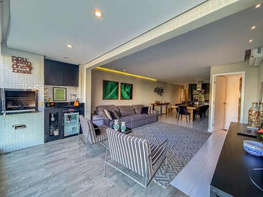 Living integrado com varanda gourmet

Área de estar ampla integrada à varanda gourmet com fechamento em vidro.

Este living contemporâneo destaca-se pela integração fluida entre a sala de estar e a varanda gourmet. O ambiente apresenta piso em porcelanato cinza, paredes em tons neutros e um amplo sofá modular cinza escuro adornado com almofadas verdes. Duas poltronas com estampa geométrica em preto e branco trazem modernidade à disposição dos móveis. A iluminação é composta por spots embutidos no teto de gesso, criando uma atmosfera acolhedora e sofisticada. A sensação é de amplitude e frescor, potencializada pela luz natural que entra pelas grandes lâminas de vidro da sacada.
