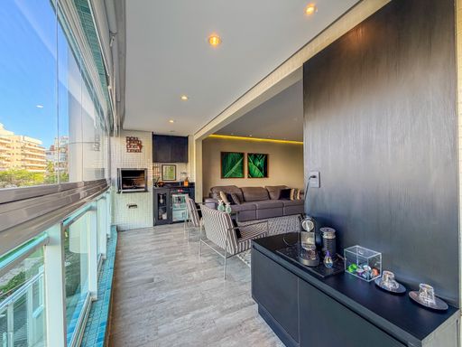 Living com painel ripado escuro

Sala de estar com poltronas decorativas e painel de madeira preto.

Nesta perspectiva do living, o destaque é a parede revestida com painel ripado em tom preto fosco, que confere elegância e profundidade ao espaço. À esquerda, a varanda integrada revela uma churrasqueira com revestimento de pastilhas cinzas. O mobiliário inclui um buffet moderno em laca preta e poltronas com padrões geométricos. A iluminação de LED embutida no teto realça as texturas da madeira e do porcelanato, criando uma estética de luxo urbano e sofisticação técnica.