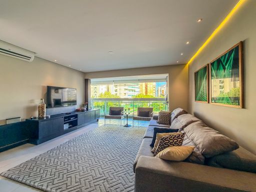 Sala de TV aconchegante

Home theater com sofá cinza, tapete geométrico e painel ripado.

Este ambiente de TV foi projetado para o máximo conforto, apresentando um sofá retrátil em tecido cinza posicionado sobre um grande tapete com estampa geométrica. O painel da TV é em laca escura, contrastando com a parede lateral em tom fendi. Quadros com folhagens verdes trazem um toque de biofilia à decoração. A iluminação indireta com sanca de LED amarela proporciona um clima íntimo e relaxante, ideal para o entretenimento doméstico.