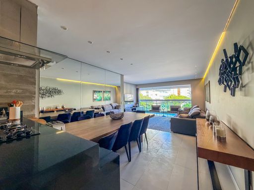 Sala de jantar integrada

Mesa de jantar para dez pessoas integrada ao living com espelho.

A sala de jantar é definida por uma imponente mesa de madeira escura com dez cadeiras estofadas em azul marinho. Uma grande parede de espelhos ao fundo duplica a sensação de espaço e reflete a iluminação decorativa do ambiente. O piso polido e a integração com a sala de estar reforçam a amplitude do imóvel. A decoração inclui objetos de vidro e metal sobre a mesa, resultando em uma estética refinada e ideal para recepções formais.