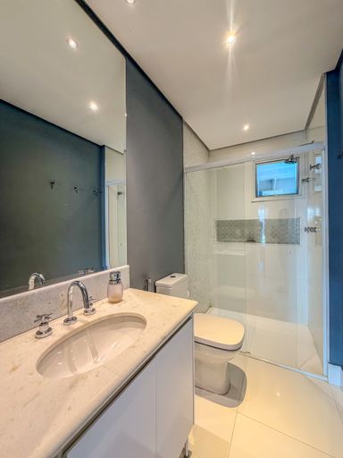 Banheiro social elegante

Banheiro com bancada de mármore claro e box de vidro.

O banheiro apresenta uma bancada em mármore creme com cuba embutida e metais cromados de design clássico. A parede principal é revestida com pintura cinza azulada, enquanto o box é delimitado por vidro transparente, revelando revestimento em pastilhas claras. O espelho amplo amplia o ambiente, que conta com iluminação embutida suave. A sensação é de limpeza, frescor e requinte funcional.