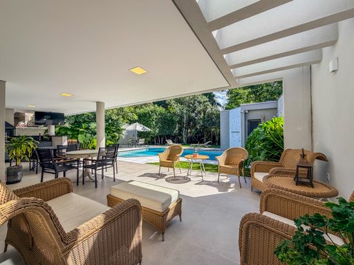 Área de lazer com sofás

Área de lazer coberta com sofás de vime e vista para a piscina.

A área de lazer coberta apresenta um design descontraído e confortável, com destaque para os sofás de vime acompanhados por almofadas texturizadas. O ambiente é integrado ao exterior por meio de portas de correr de vidro, que revelam a piscina e o jardim arborizado. O piso é em porcelanato claro, e as paredes são brancas. A iluminação é suave, com pontos de luz embutidos no teto. O ambiente transmite frescor e conforto.