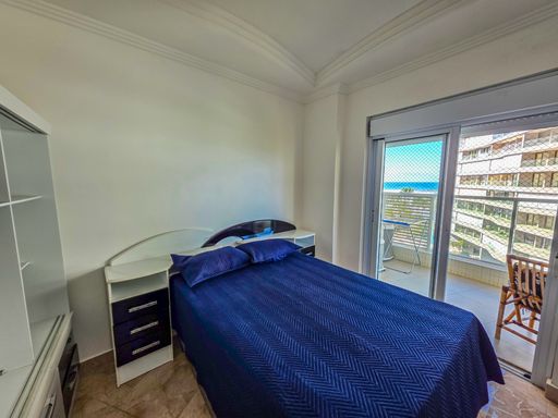 Dormitório casal com vista mar.

Quarto de casal com cama azul e acesso direto à varanda.

O quarto principal oferece uma experiência de relaxamento única, com uma cama de casal vestida em azul marinho e acesso direto à varanda por uma grande porta de vidro. Através da abertura, é possível ver o azul do mar e o horizonte, integrando a paisagem ao ambiente de descanso. O teto possui design em gesso e luminárias embutidas. A estética é leve e arejada, permitindo que a brisa marinha circule livremente, garantindo uma temperatura sempre fresca e agradável.