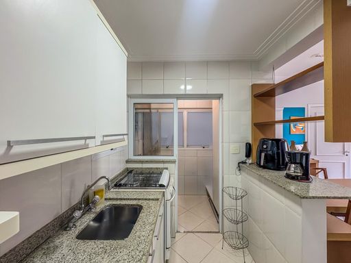 Área de serviço e cozinha integradas

Visão da bancada de granito com fogão embutido e acesso à área de serviço.

Este ângulo mostra a continuidade da cozinha em direção à área de serviço. A bancada de granito estende-se para abrigar o cooktop e a pia, com revestimento de azulejos brancos que facilita a limpeza. À direita, um balcão de apoio com cafeteira e utensílios organiza o espaço. A iluminação natural vinda da janela ao fundo mantém o ambiente arejado. A combinação de materiais frios como pedra e cerâmica ajuda a manter a temperatura baixa em áreas de cocção.