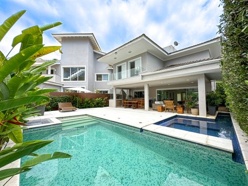 Fachada com piscina e jardim

Área externa de casa de luxo com piscina de pastilhas esverdeadas e jardim tropical.

Esta impressionante área de lazer externa apresenta uma grande piscina revestida com pastilhas em tons de verde-água, cercada por um amplo deck de pedra clara antitérmica. Ao fundo, ergue-se a imponente fachada de uma residência de dois pavimentos em tom cinza-claro, com grandes vãos envidraçados e varanda coberta integrada. O paisagismo é marcado por folhagens tropicais densas e coqueiros nas laterais, que conferem privacidade ao espaço. O ambiente evala frescor, sofisticação e uma atmosfera exclusiva de veraneio ou descanso de alto padrão.