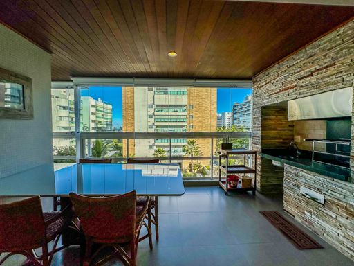 Varanda envidraçada com vista externa.

Espaço gourmet em varanda com fechamento de vidro e vista da cidade.

A imagem destaca a integração da varanda com a paisagem urbana, proporcionada pelas amplas lâminas de vidro que garantem segurança e isolamento sem perder a luminosidade. O piso cerâmico de fácil manutenção estende-se até a área de lazer, onde a marcenaria planejada abriga utensílios e uma bancada de apoio em pedra. O contraste entre o teto de madeira escura e as paredes claras reforça a estética moderna do projeto. É um ambiente que transmite bem-estar e sofisticação, com excelente controle térmico e acústico.