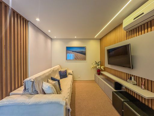 Sala de home theater aconchegante

Sofá claro com almofadas em frente ao painel de TV de madeira.

Esta moderna sala de TV destaca-se pelo design sofisticado e conforto térmico. O ambiente conta com um longo sofá em tom bege claro decorado com almofadas azuis e brancas, posicionado sobre um grande tapete felpudo marrom. A parede oposta é inteiramente revestida por um painel de madeira ripada texturizada, que abriga uma televisão de tela plana instalada em um suporte branco, além de um rack cinza com pufes embutidos. O projeto de iluminação de gesso apresenta spots embutidos e uma fita de LED linear embutida que banha a parede com luz quente e acolhedora. Um aparelho de ar-condicionado garante o clima agradável do espaço.