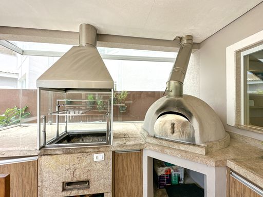 Churrasqueira e forno de pizza

Bancada de granito com coifas de inox, churrasqueira moderna e forno de pizza.

Focada exclusivamente na área de cocção, esta imagem destaca o acabamento de alta qualidade da churrasqueira com espetos giratórios e do forno de pizza artesanal revestido de cimento queimado. Ambos os equipamentos são coroados por tubulações e coifas industriais de aço inox escovado que sobem em direção ao teto. A bancada de granito ocre oferece uma ampla superfície de apoio para o churrasqueiro, combinando praticidade, higiene e um design moderno voltado para o lazer de alto padrão.