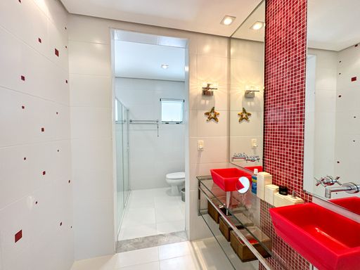 Lavabo moderno com cuba vermelha

Lavabo com cuba de apoio vermelha vibrante, bancada de vidro e espelho grande.

Este lavabo contemporâneo destaca-se pelo uso de cores ousadas e superfícies reflexivas. Uma imponente cuba de apoio retangular em tom vermelho translúcido está posicionada sobre uma bancada de vidro temperado com estrutura metálica. A parede atrás da pia é revestida com pastilhas de vidro vermelhas, criando um plano de fundo vibrante e sofisticado. Um grande espelho vertical se estende até o teto, ampliando o espaço e refletindo a iluminação embutida. Ao fundo, uma porta aberta revela a continuidade para a área do box de banho em tons claros, estabelecendo um contraste térmico e estético marcante.
