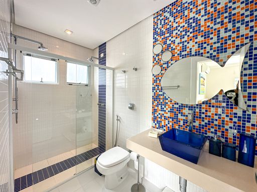 Banheiro moderno com cuba azul

Banheiro com pia bege, cuba de apoio azul quadrada e parede de mosaico colorido.

Este banheiro contemporâneo destaca-se pelo uso de elementos vibrantes e geométricos. A bancada suspensa em quartzo bege claro acomoda uma cuba de apoio quadrada em vidro azul cobalto. A parede ao fundo da pia é inteiramente revestida por pastilhas multicoloridas em tons de azul, laranja, branco e preto, criando um forte ponto focal. Um espelho circular com moldura discreta complementa a área do lavatório. O box possui fechamento em vidro temperado transparente e piso com detalhes em pastilhas escuras, resultando em uma estética litorânea sofisticada, limpa e cheia de personalidade.