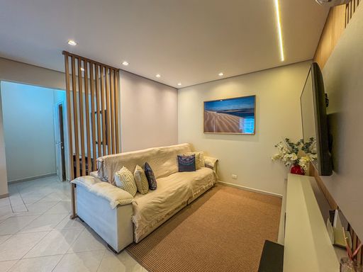 Sala de estar com painel ripado

Sofá com almofadas em sala iluminada por LED e divisória de madeira.

Uma visão em perspectiva da sala de estar residencial evidenciando a elegante integração espacial. O sofá de tecido claro com almofadas estampadas divide harmonicamente a área com uma divisória vertical de madeira vazada ao fundo, que delimita o hall sem bloquear a luz. A parede dos fundos recebe um quadro decorativo com fotografia de praia, em perfeita sintonia com a paleta de cores neutras do porcelanato e das paredes pintadas de bege. A fita de iluminação embutida no teto e os spots direcionais proporcionam uma estética contemporânea, intimista e muito convidativa.