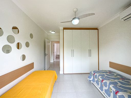 Quarto de solteiro funcional amplo

Quarto com duas camas de solteiro, armário planejado branco e ventilador de teto.

Este dormitório de solteiro apresenta uma disposição inteligente com duas camas posicionadas nas extremidades opostas do ambiente, uma coberta com colcha amarela vibrante e a outra com estampa cinza e azul. Ao fundo, um grande armário planejado branco com portas de abrir estende-se até o teto com acabamento em madeira clara nas laterais. Detalhes decorativos circulares espelhados enfeitam a parede acima de uma das camas. O teto possui sanca de gesso e um ventilador de teto moderno com luminária integrada, mantendo o ambiente fresco, arejado e bem iluminado.