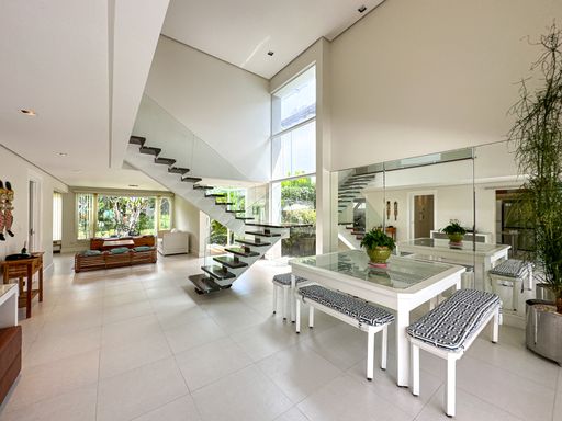 Sala de jantar com pé-direito duplo

Sala de jantar com mesa branca, bancos estofados e escada vazada ao fundo.

Esta magnífica sala de jantar destaca-se pela imponência do seu pé-direito duplo e arquitetura monumental. Ao centro, encontra-se uma mesa de jantar branca com tampo de vidro, acompanhada por bancos longos estofados com estampa em zigue-zague preta e branca. Ao fundo, uma imponente escada com degraus flutuantes de madeira e guarda-corpo de vidro leva ao piso superior. Uma enorme parede de espelhos duplica a sensação de amplitude do espaço, que recebe luz natural massiva pelas altas vidraças. O ambiente transmite extremo luxo, modernidade e fluidez espacial.