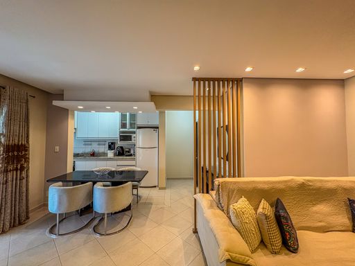 Ambiente integrado com cozinha americana

Divisória ripada conectando a sala de estar à mesa de jantar.

Perspectiva que revela a transição fluida entre a sala de estar, a mesa de jantar e a cozinha planejada. Em primeiro plano, o braço do sofá com almofadas estampadas amarelas e azuis estabelece o limite da área de TV. Uma estrutura ripada de madeira maciça atua como elemento arquitetônico divisório. Ao fundo, a mesa de jantar com tampo de vidro escuro é acompanhada por cadeiras estofadas modernas com base metálica curva, integrando-se diretamente à cozinha americana branca equipada com geladeira e armários sob medida.