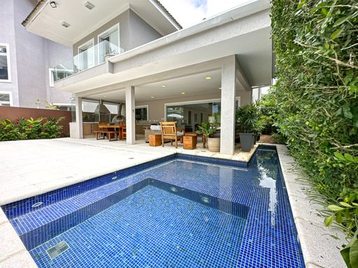 Piscina integrada com área gourmet

Piscina em formato L revestida com pastilhas escuras integrada à varanda.

Esta perspectiva destaca a piscina em formato geométrico revestida com pastilhas azuis reflexivas, localizada bem ao lado da área social coberta da casa. O deck de pedra conecta diretamente a água à varanda gourmet. O andar superior da residência possui guarda-corpo de vidro temperado e alumínio anodizado, reforçando a arquitetura contemporânea. O paisagismo lateral conta com uma parede verde de arbustos densos, conferindo privacidade, frescor e isolamento térmico natural ao ambiente de lazer.
