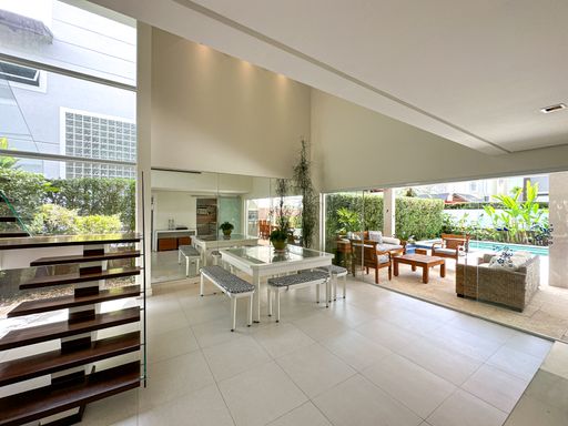 Integração total da área social

Sala com mesa de jantar branca integrada à área de lazer externa da piscina.

Esta perspectiva a partir da escada revela a conexão total entre a sala de jantar e a área gourmet externa. A parede espelhada reflete a mesa branca com seus bancos de design contemporâneo. Através dos grandes vãos abertos e portas de correr totalmente recolhidas, o ambiente interno se funde com um deck de madeira coberto, equipado com poltronas e mesas externas, culminando na vista para a piscina. A transição perfeita elimina barreiras, criando um living ideal para recepções luxuosas e descontraídas em dias quentes.