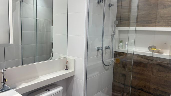 banheiro social com box de vidro e nicho, com amplo espelho valorizando ambiente