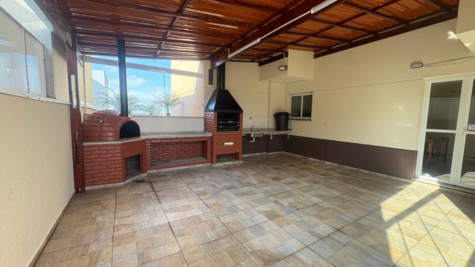 Amplo espaço gourmet envidraçado com churrasqueira a carvão e forno a lenha
