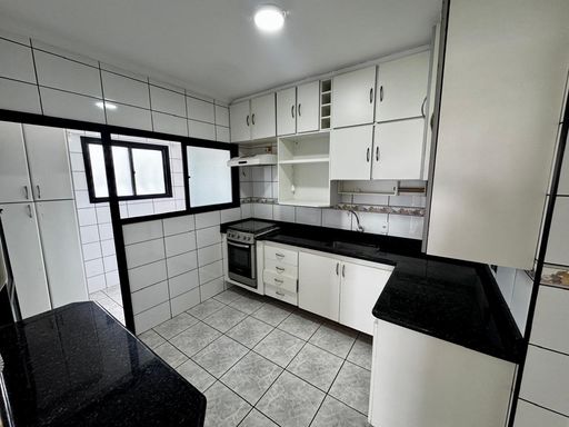 cozinha com armários planejados com ampla pia em granito preta, semi integrada a área de serviço bem arejada