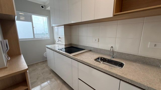 cozinha com armários planejados, fogão de infusão e ampla pia em granito, semi integrada a área de serviço bem arejada