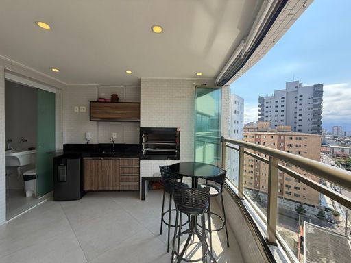 ampla varanda gourmet envidraçada com cortina blackout, churrasqueira a carvão e ampla pia em granito com armários planejados