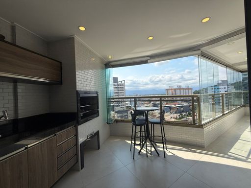 ampla varanda gourmet envidraçada com cortina blackout, churrasqueira a carvão e ampla pia em granito com armários planejados