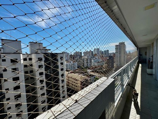 ampla varanda gourmet com pequena vista mar, com tela de proteção e acesso as suítes