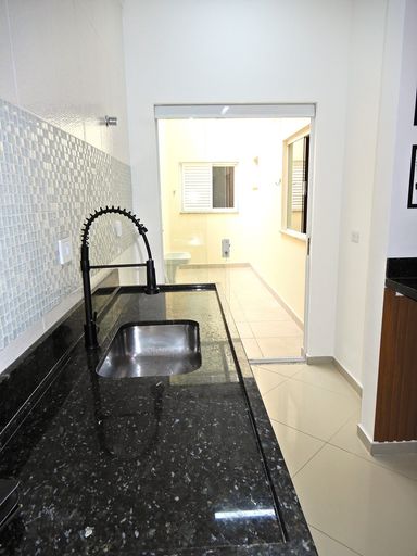 Cozinha com pia em granito preta, semi integrada a área de serviço com porta de correr de vidro, bem arejada e iluminada