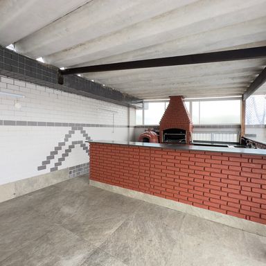 Área do salão de festas com churrasqueira e forno de pizza.