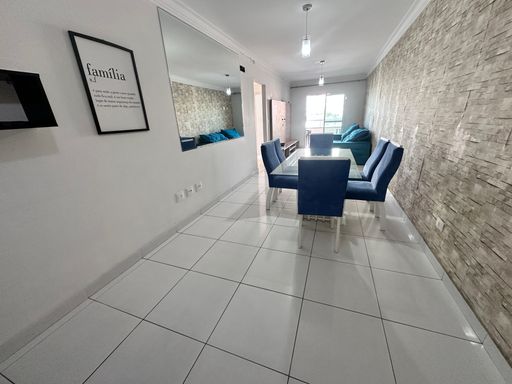 Sala com dois ambientes, equipada com sofá, painel de TV, mesa de jantar para seis pessoas e espelho de parede.