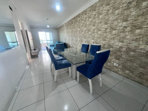 Sala com dois ambientes, equipada com sofá, painel de TV, mesa de jantar para seis pessoas e espelho de parede.