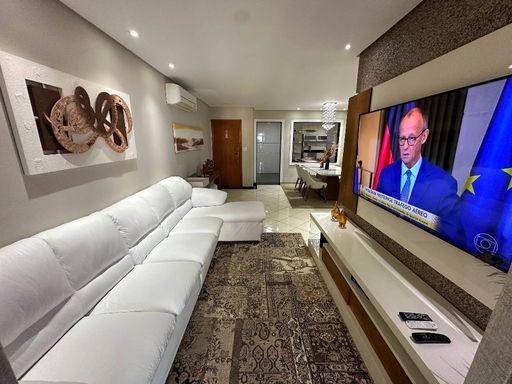 Sala com dois ambientes, sofá branco e acesso à sacada gourmet.