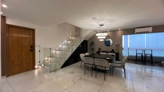 Sala ampla com dois ambientes, lustre pendente, mesa de oito lugares e ar-condicionado.