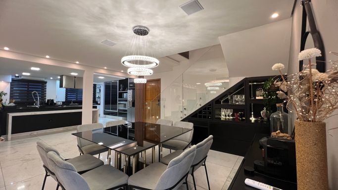 Sala ampla com dois ambientes, lustre pendente, mesa de oito lugares e ar-condicionado.