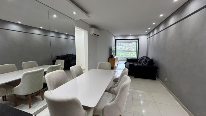 Sala com dois ambientes, equipada com mesa de jantar para seis lugares, sofá, parede espelhada e ar-condicionado.