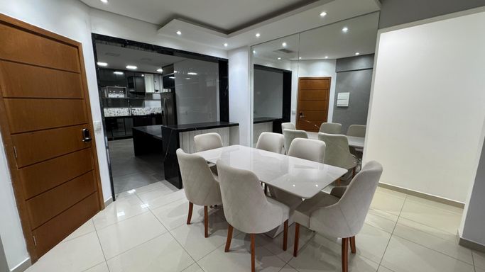 Sala com dois ambientes, equipada com mesa de jantar para seis lugares, sofá, parede espelhada e ar-condicionado.
