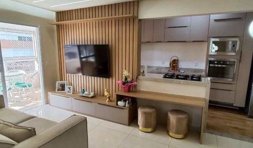 Sala de dois ambientes com um sofá, painel de TV e sacada gourmet.